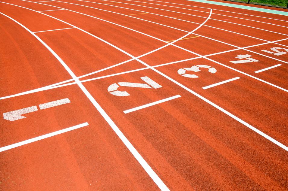 Nahaufnahme einer roten Laufbahn mit weißen Startnummern 1, 2, 3 und Markierungen für Laufstrecken.